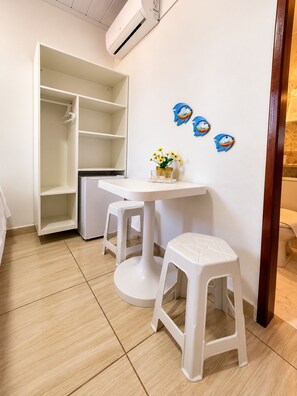 A room with a white wardrobe, a small table with a vase of flowers, and two white stools.