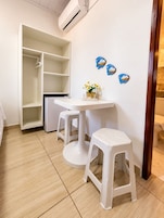 Quarto com guarda-roupa branco, uma mesinha com um vaso de flores e dois banquinhos brancos.