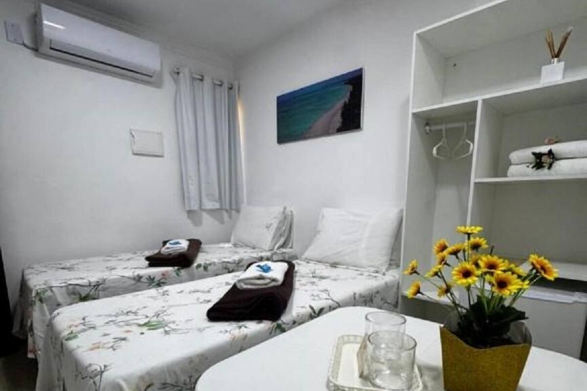 Une chambre d’hôtel avec deux lits, une petite table avec un verre et un vase de fleurs, une étagère avec des serviettes et un tableau au mur.