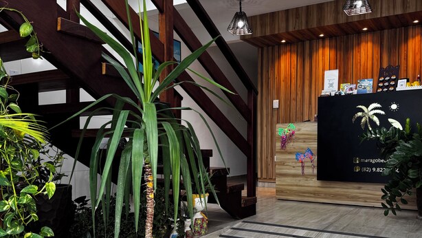 Un área de recepción con una escalera de madera, plantas en macetas, un mostrador de recepción y un piso con diseño.