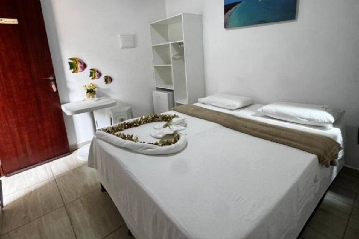 Une chambre d’hôtel propre et moderne, avec un lit, une petite table de chevet, une armoire blanche et un tableau au mur.