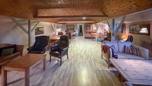 Een ruime kamer met houten plafond, een zithoek met tafel en stoelen, een bank en een lamp.