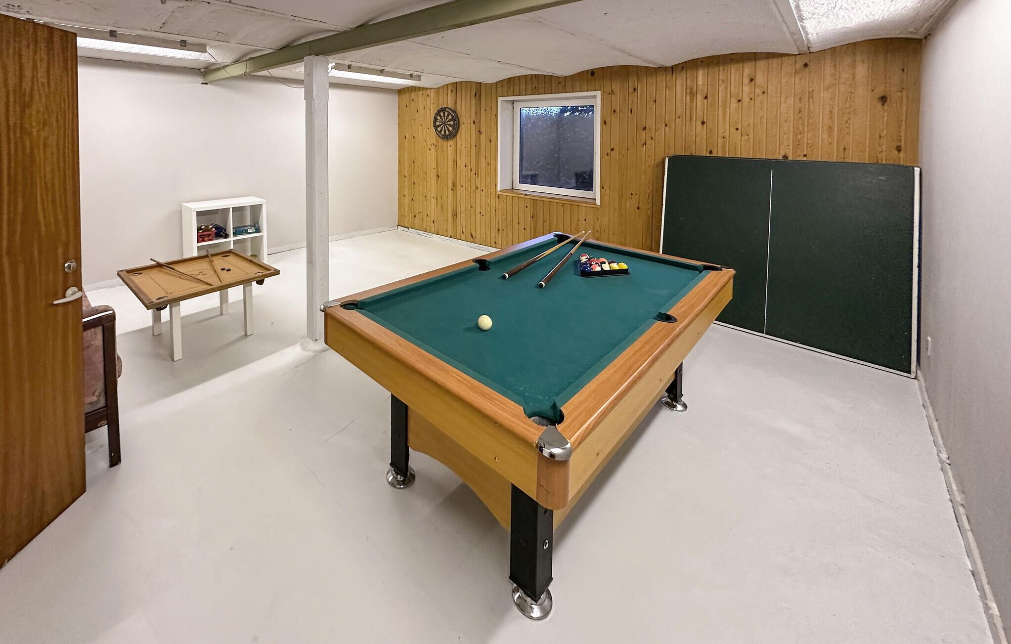 Ein Billardtisch mit Kugeln und Spielstangen, eine Dartscheibe und ein Fenster mit Blick.