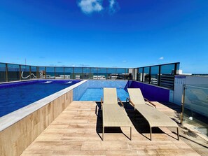 En pool på taket med två solstolar och ett område intill poolen.