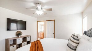 A bedroom with a bed, a TV mounted on the wall, a ceiling fan, and a door leading to a bathroom.