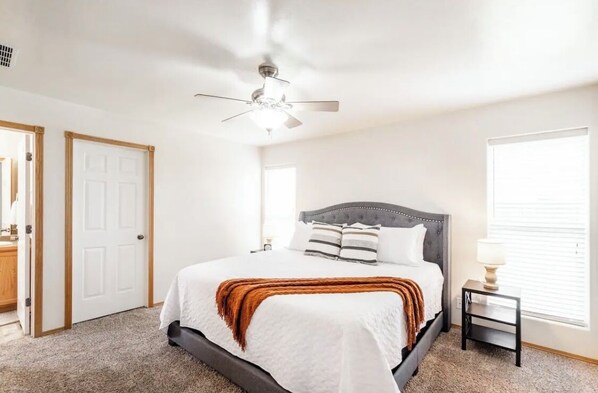A bedroom with a bed, a ceiling fan, a nightstand, and a window.