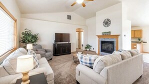 A spacious living room with a fireplace, a television, and a ceiling fan.