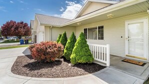 A single-story house with a front porch, a garage, and a small front yard with trimmed bushes and a tree.