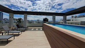 Zona de piscina en la azotea con sillones de descanso y vistas al horizonte de la ciudad.