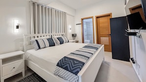 Una habitación de hotel moderna con una cama grande, una mesita de noche, un televisor de pantalla plana y zona de ducha.