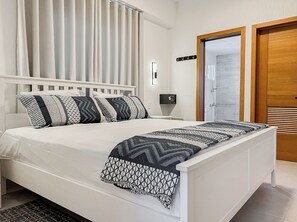 Una cama bien hecha con almohadas estampadas, una mesita de noche con lámpara y una puerta de madera con espejo.