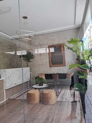 Un vestíbulo moderno con una recepción de mármol, un área de descanso con sofá y pufs, una gran planta en maceta y una obra de arte enmarcada en la pared.