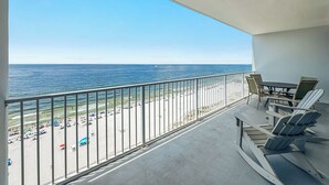 Een balkon met uitzicht op het strand en de oceaan. Er staan stoelen en een tafel op het balkon.