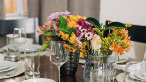 A dining table set with clear glassware, white plates, and a vase with colorful flowers.