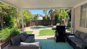 A covered patio with wicker furniture, a pool, and a view of the backyard.