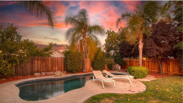 A backyard with a swimming pool, lounge chairs, and a wooden fence.