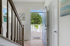 A wooden staircase leading to a deck with a white railing, a door with a keypad lock, and a painting of a lighthouse on the wall.