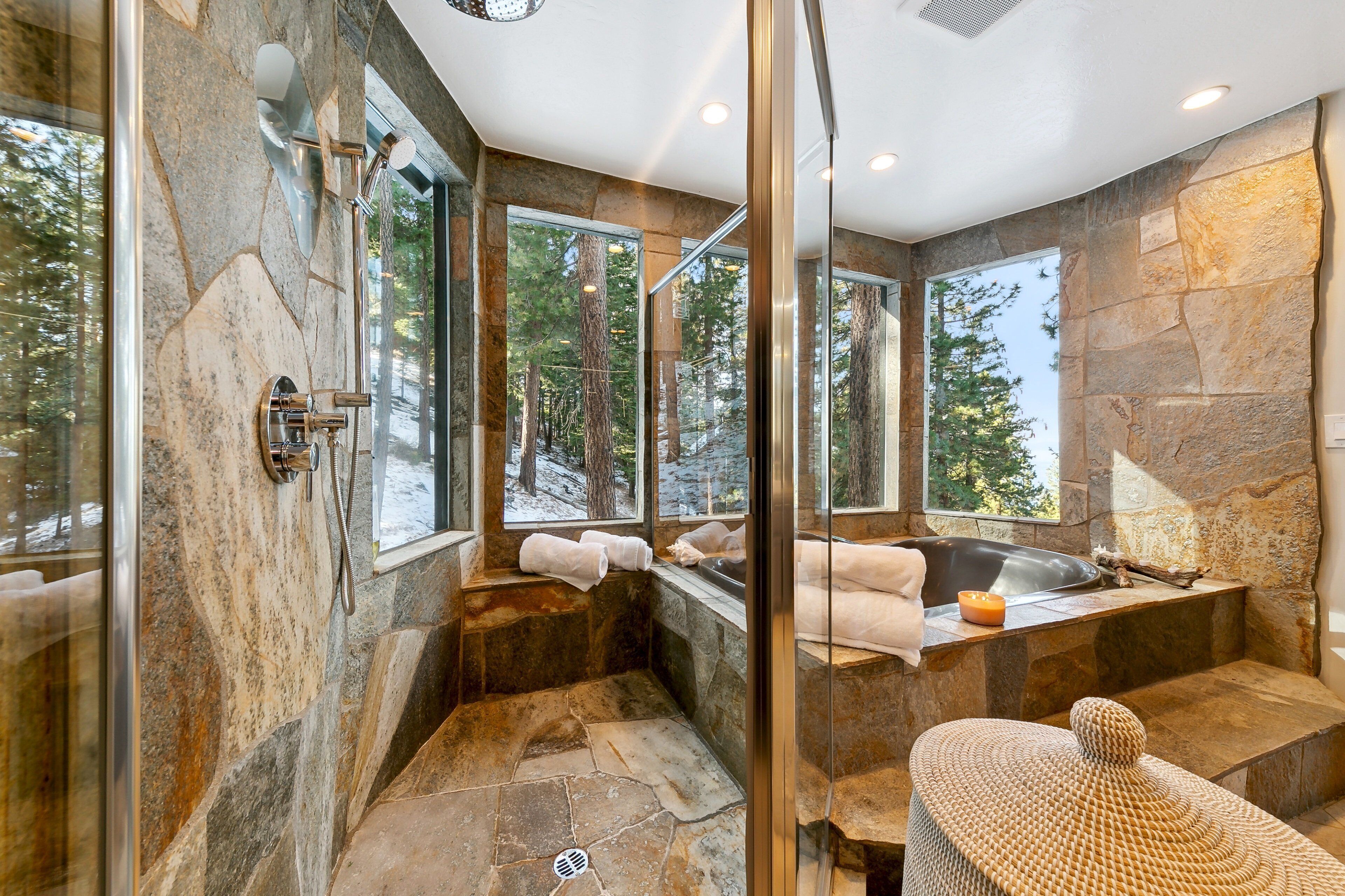 Un baño moderno con paredes de piedra, cabina de ducha de vidrio y una bañera grande.