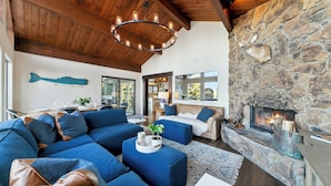 A cozy living room with a stone fireplace, blue sofas, and a wooden ceiling.