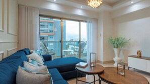 A modern living room with a sectional sofa, a round wooden coffee table, and a view of the city through large windows. - Amazing Harmony Apt 12FLR in LaJulia @Pool*Gym*Spa (Santo Domingo)