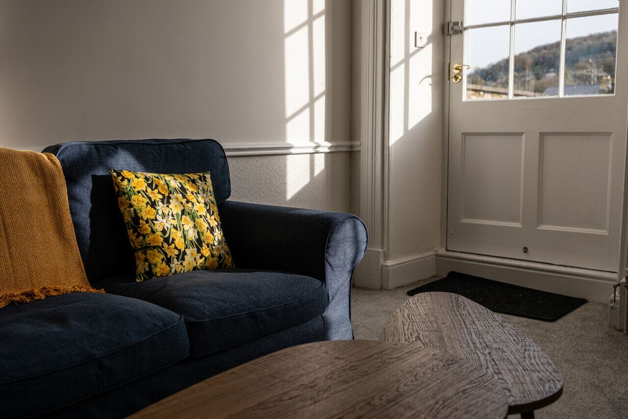 A living room with a dark blue sofa, a yellow floral pillow, and a brown throw blanket.