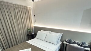 A modern hotel room with a neatly made bed, a small table with a chair, and a wall-mounted lamp. - Melhores Flats (João Pessoa)