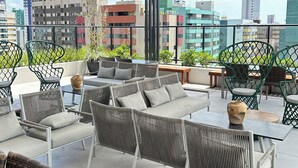 A rooftop terrace with outdoor seating, a view of the city skyline, and modern architecture. - Melhores Flats (João Pessoa)