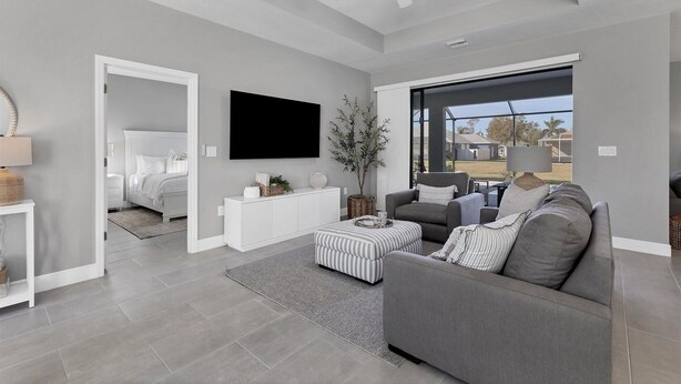 A modern living room with a grey sofa, a flat-screen TV, and a large window offering a view of the outdoors. - Punta Gorda Private Pool Vacation Home (Punta Gorda)