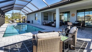 A covered outdoor swimming pool area with lounge chairs and a table, surrounded by a glass enclosure. - Punta Gorda Private Pool Vacation Home (Punta Gorda)