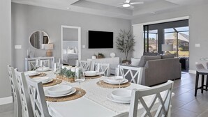 A dining area with a white table set for six, a ceiling fan, and a large window offering a view of the outdoors. - Punta Gorda Private Pool Vacation Home (Punta Gorda)