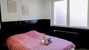 A bed with a pink bedspread, a rolled-up towel, and a welcome bag on it. There are two framed floral artworks on the wall above the bed. - “black studio”, wifi, Bollaert, 3 pers, RDC (Lens)