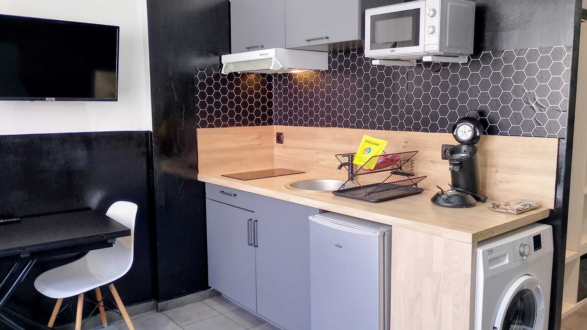 Een kleine keuken met een magnetron, koffieapparaat, spoelbak en een wasmachine.