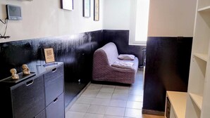 A room with a dark-colored sofa, a small cabinet with drawers, a framed QR code, and a wall-mounted device. - “black studio”, wifi, Bollaert, 3 pers, RDC (Lens)