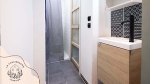 Une petite salle de bain avec une douche, un lavabo blanc doté d’un robinet noir et des carreaux décoratifs sur le mur.