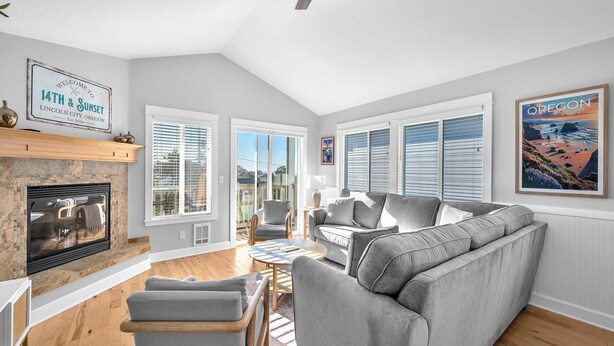 Ein geräumiges Wohnzimmer mit Kamin, grauen Sofas und einem großen Fenster mit Jalousien.