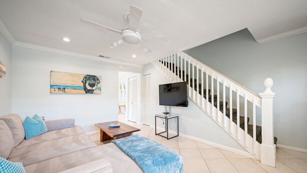 A living room with a beige sofa, a coffee table, a TV on a stand, and a staircase with white railings.