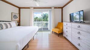 A bedroom with a bed, a chair, a dresser, a television, and a balcony with a view of trees.