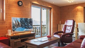 A cozy living room with a wooden interior, a large flat-screen TV, leather sofas, and a balcony with a mountain view. - Moulin du Raé A2 by Interhome (Nendaz)