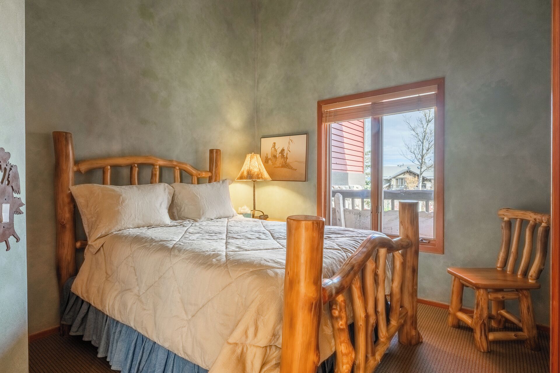 A bedroom with a wooden bed frame, a bedside lamp, and a window with a view of the outside.