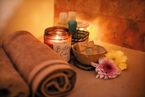 A spa setting with a candle, rolled towels, a bowl, and flowers.