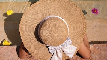 Una persona sentada junto a una piscina, con sombrero de paja y lazo, rodeada de flores.