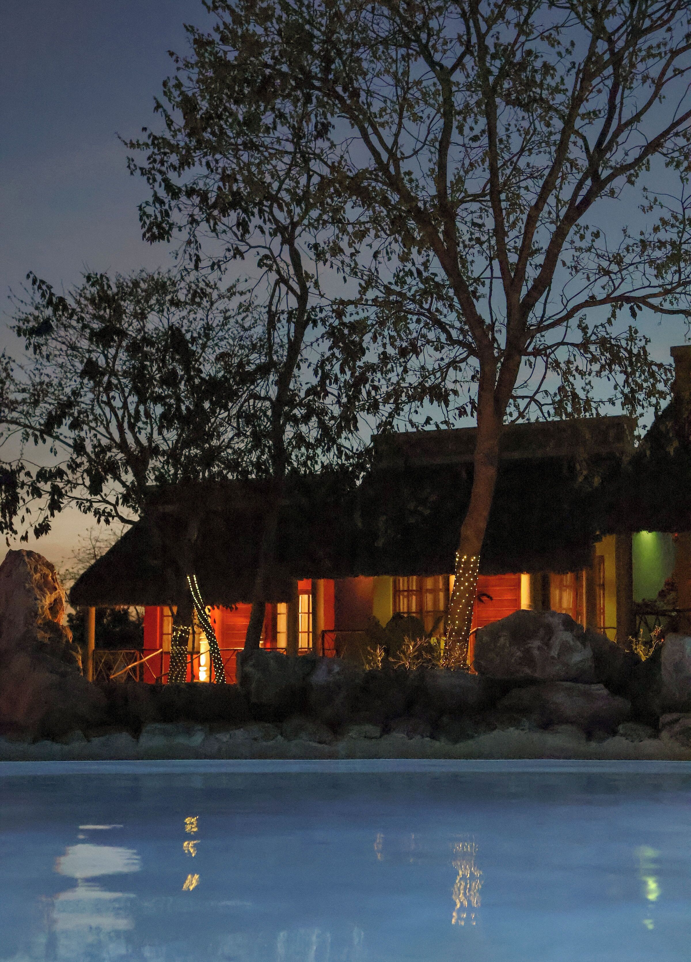 A building with a thatched roof, surrounded by rocks and trees, with a pool in the foreground.