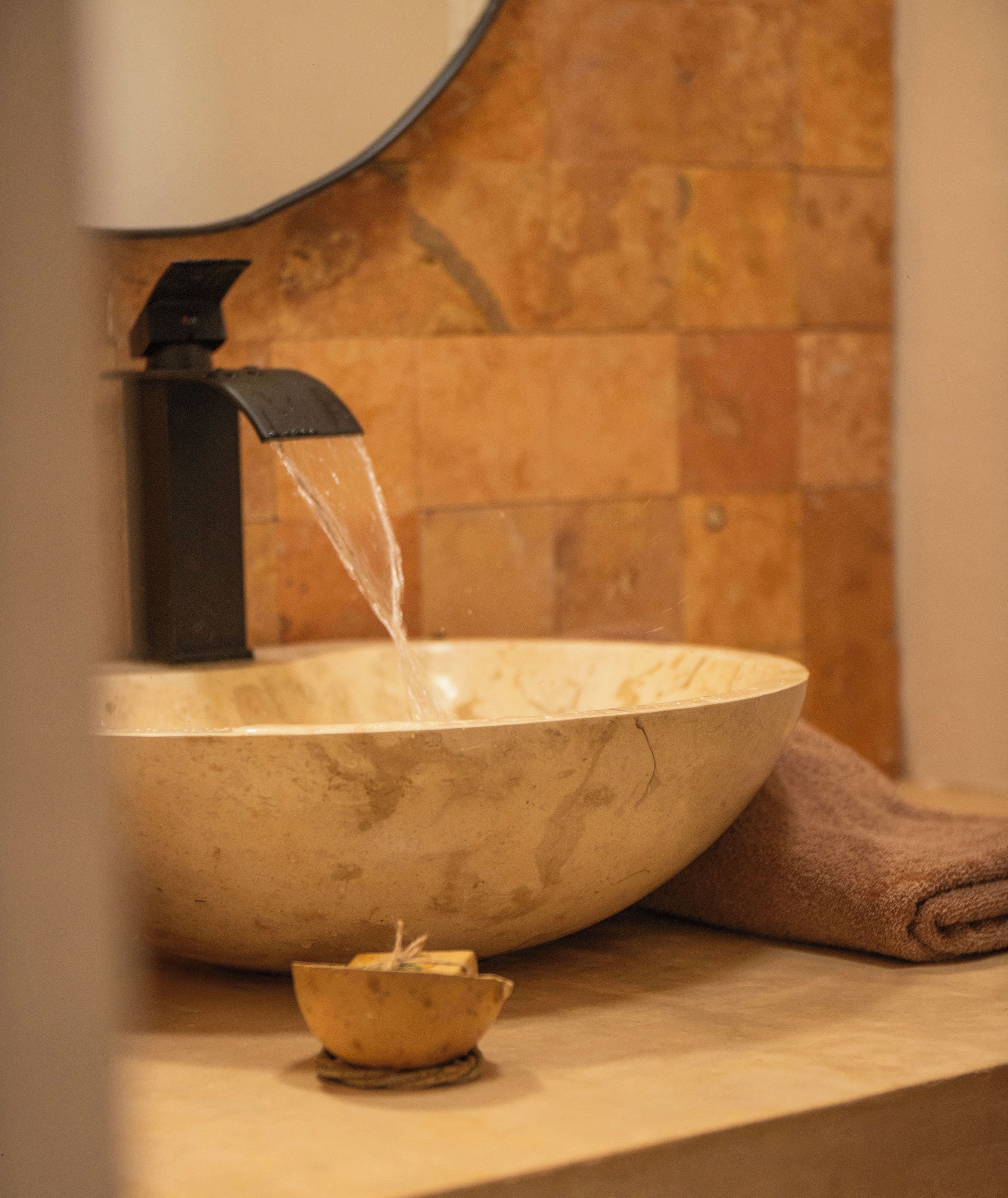 Un lavabo de baño con una pila de mármol, un grifo y un recipiente pequeño.