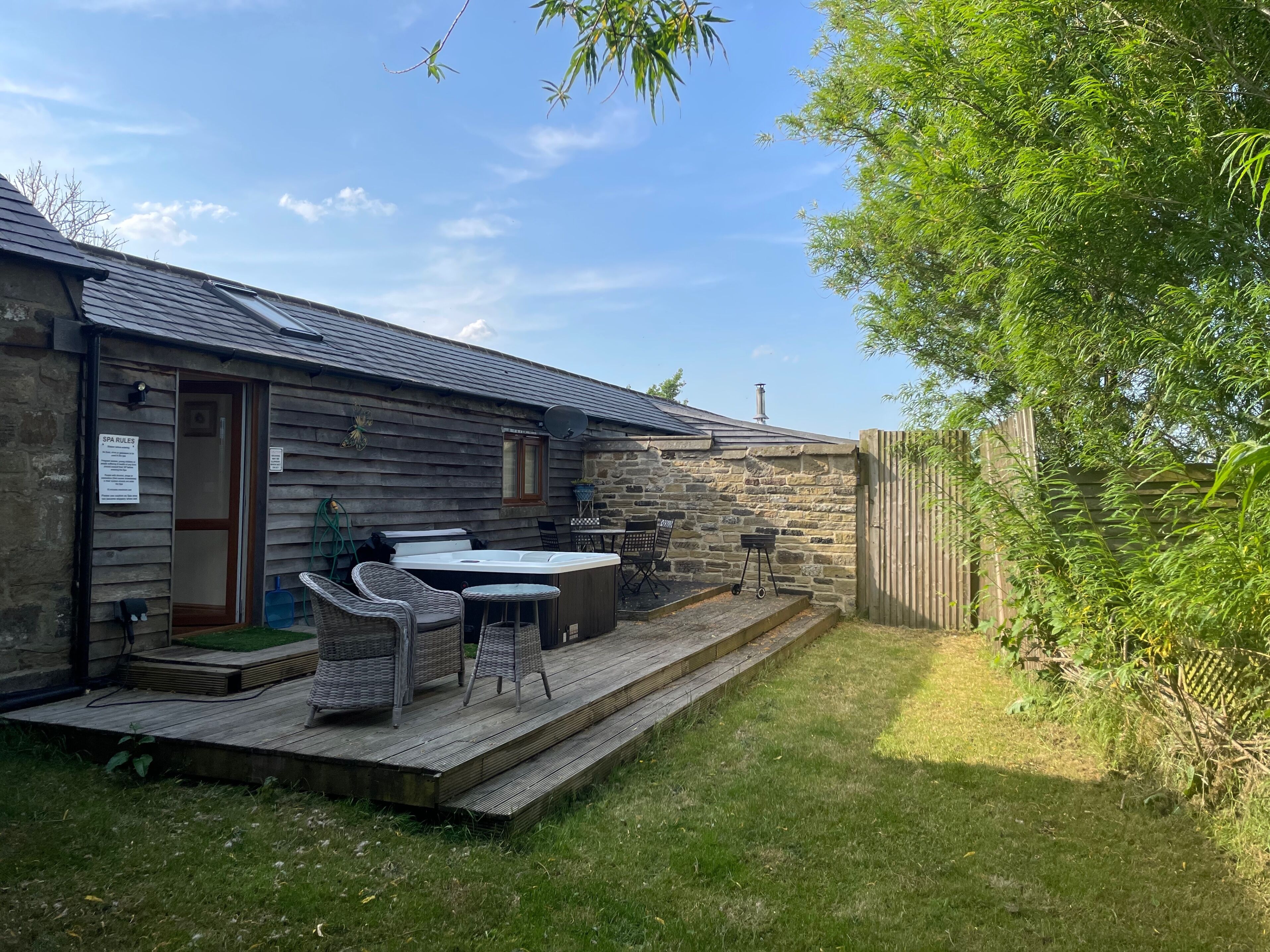 A stone cottage with a wooden deck, outdoor seating, and a hot tub.