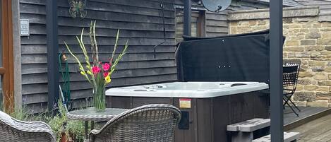 An outdoor patio with wicker furniture, a hot tub, and a pergola.