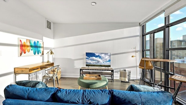 A modern living room with a blue sofa, a wooden coffee table, a TV, and a large window.