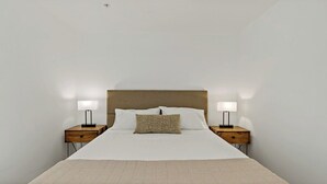 A neatly made bed with a wooden headboard, two bedside tables with lamps, and a single decorative pillow. - Downtown |Views | Luxury | Sunny (Washington)