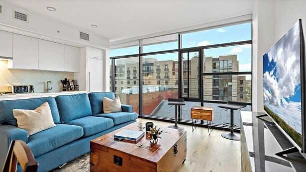 A modern living room with a blue sofa, a wooden coffee table, and a large window offering a city view. - Downtown |Views | Luxury | Sunny (Washington)