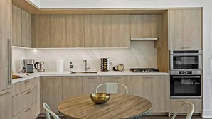 Une cuisine moderne avec des meubles en bois, une table de salle à manger ronde et des appareils électroménagers intégrés, notamment une cuisinière et un four.