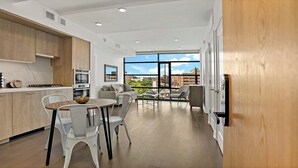 Une cuisine moderne avec des meubles blancs, un coin repas comprenant une table et des chaises, et une grande fenêtre offrant une vue sur la ville.
